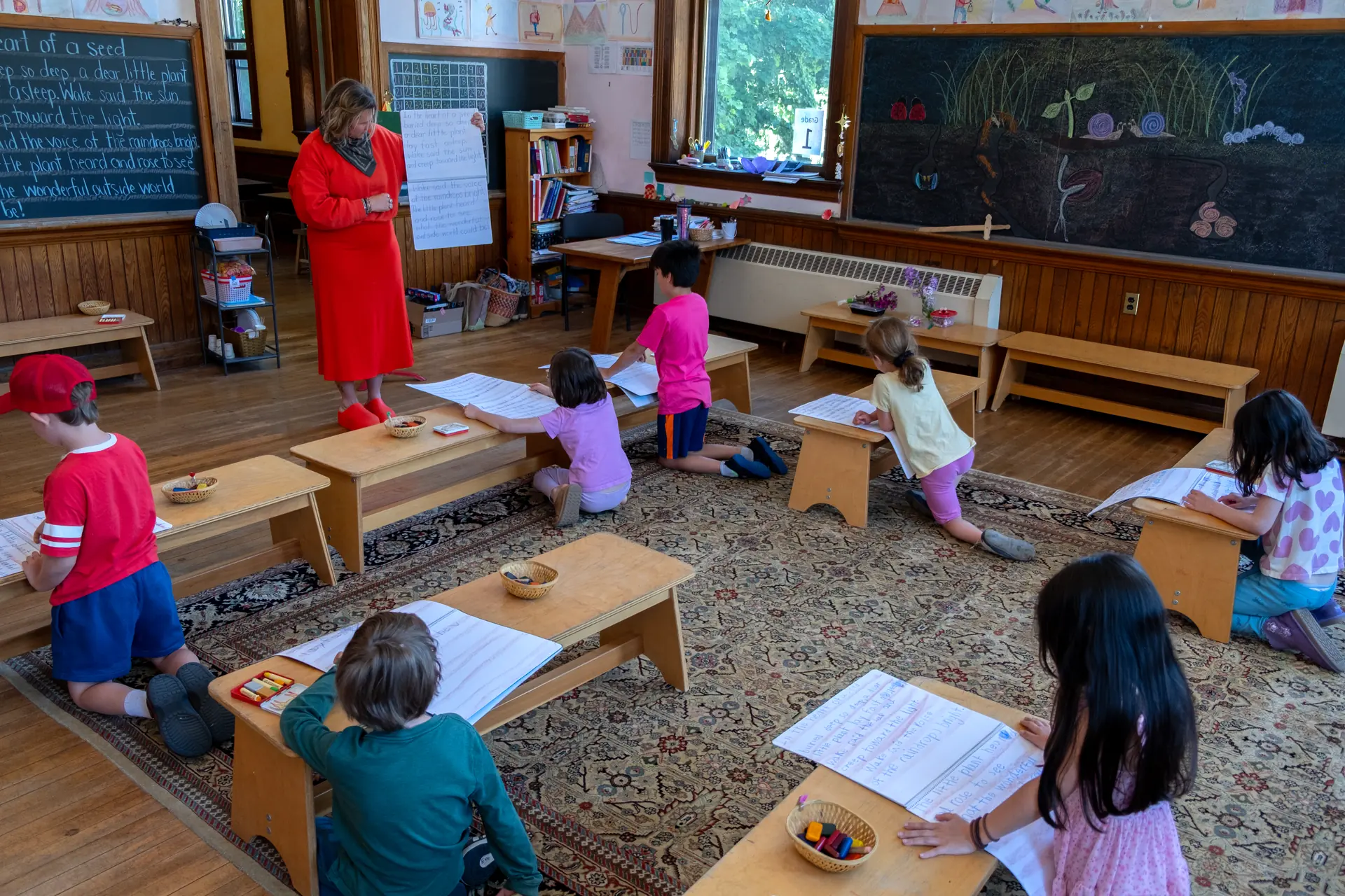 First-grade students writing in main lesson books around their teacher