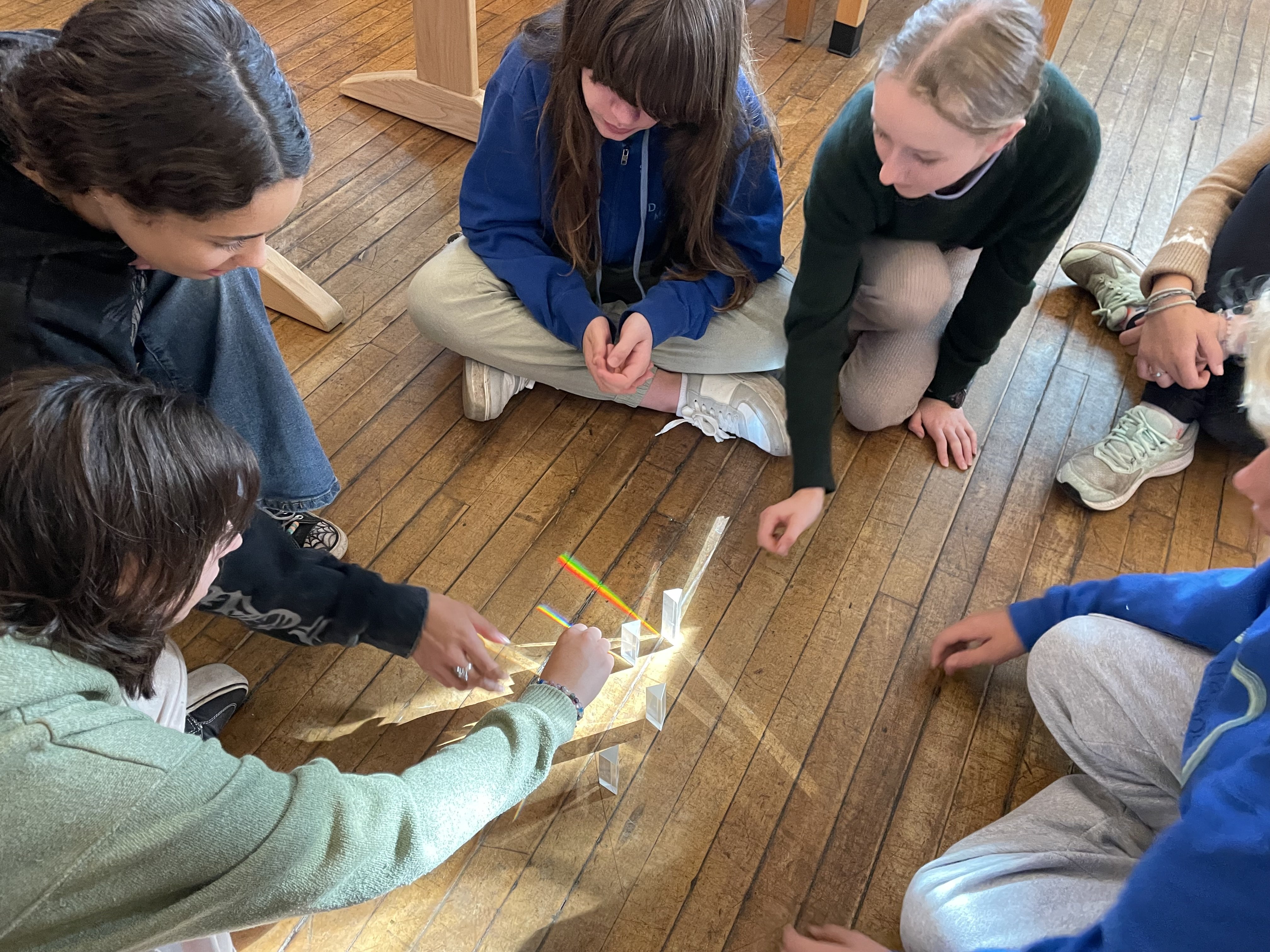 Middle school students exploring light refraction with prisms on the classroom floor