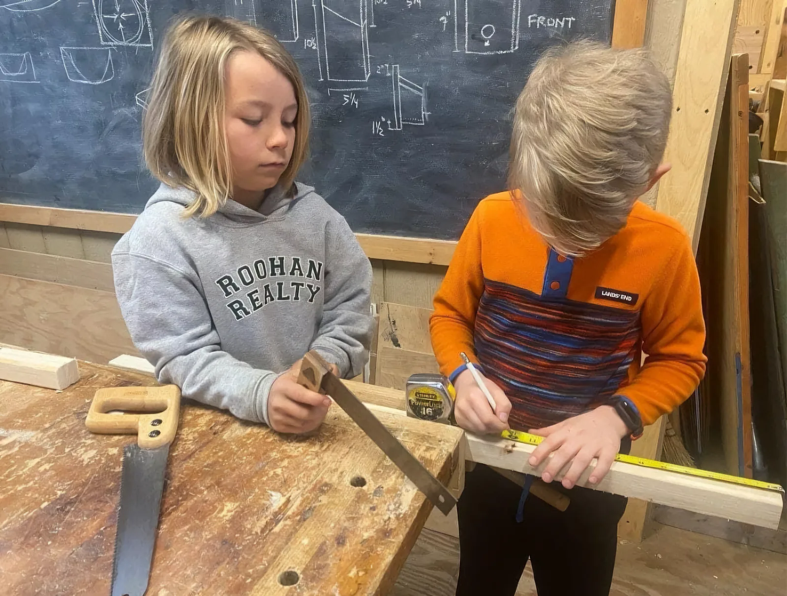 Two students working with saws and measuring tape in the woodworking workshop