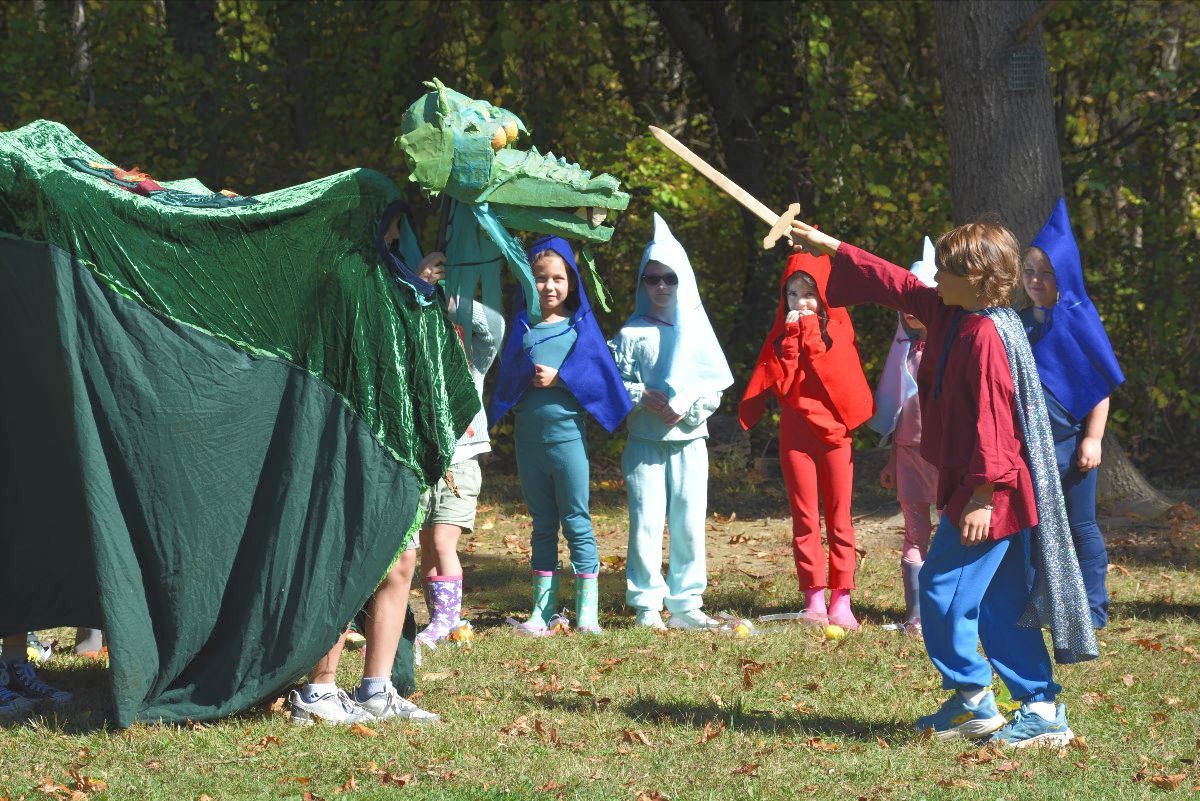 Students in colorful capes acting out the Michaelmas story with a large dragon puppet
