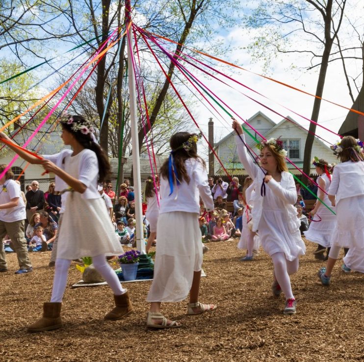Students in white dresses dancing the Maypole with ribbons