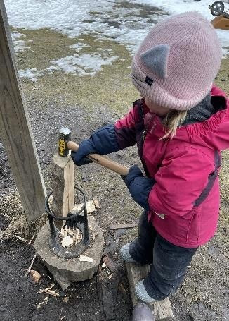 A young child splitting kindling with a mallet outdoors