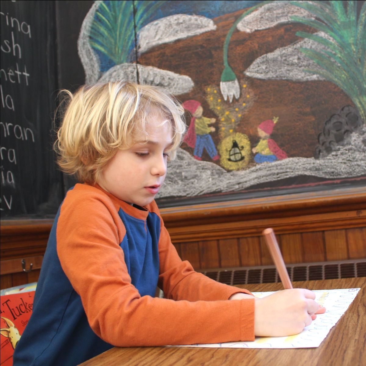 A young student writing at a desk in front of a chalkboard