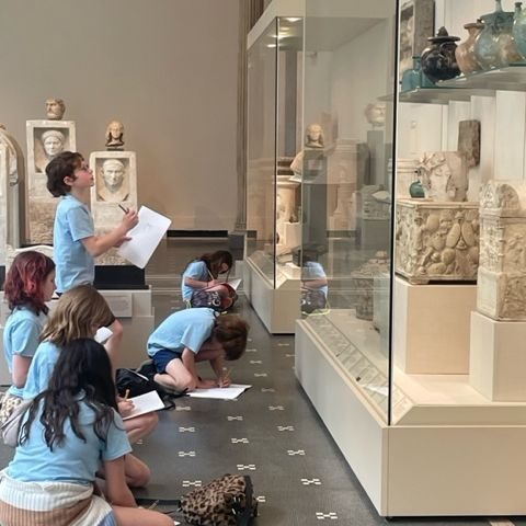Students sketching artifacts among the display cases at a museum