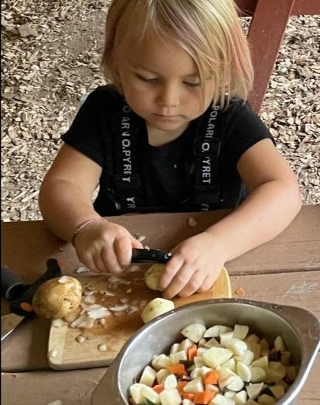 A young child steadying a potato with one hand and peeling it with the other
